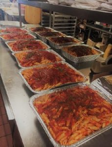 Trays of pasta are lined up in a kitchen.