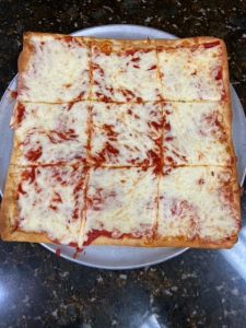A square pizza on a plate with cheese on it.